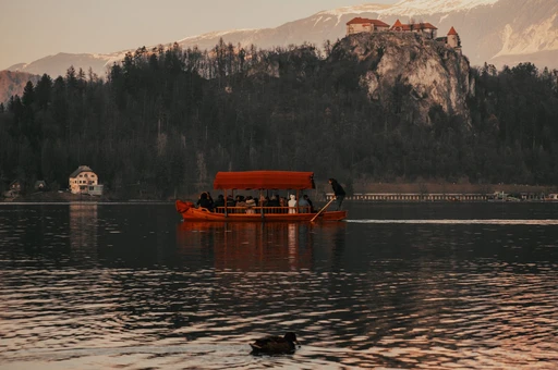 A traditional Pletna boat glides across Lake Bled with a view of Bled Castle amidst a serene landscape.