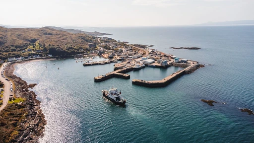 Stunning aerial shot of Mallaig harbor with boats and rugged coastline under a sunny sky.