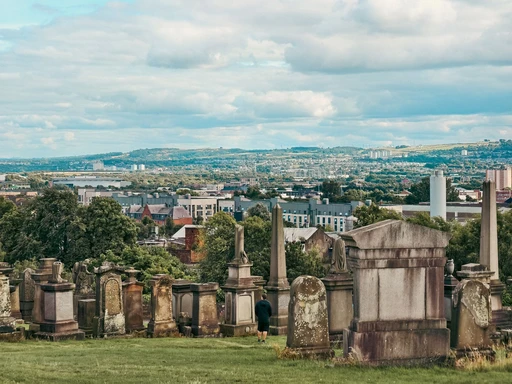 Weathered monuments on the Glasgow Necropolis hill with the city spread out behind.