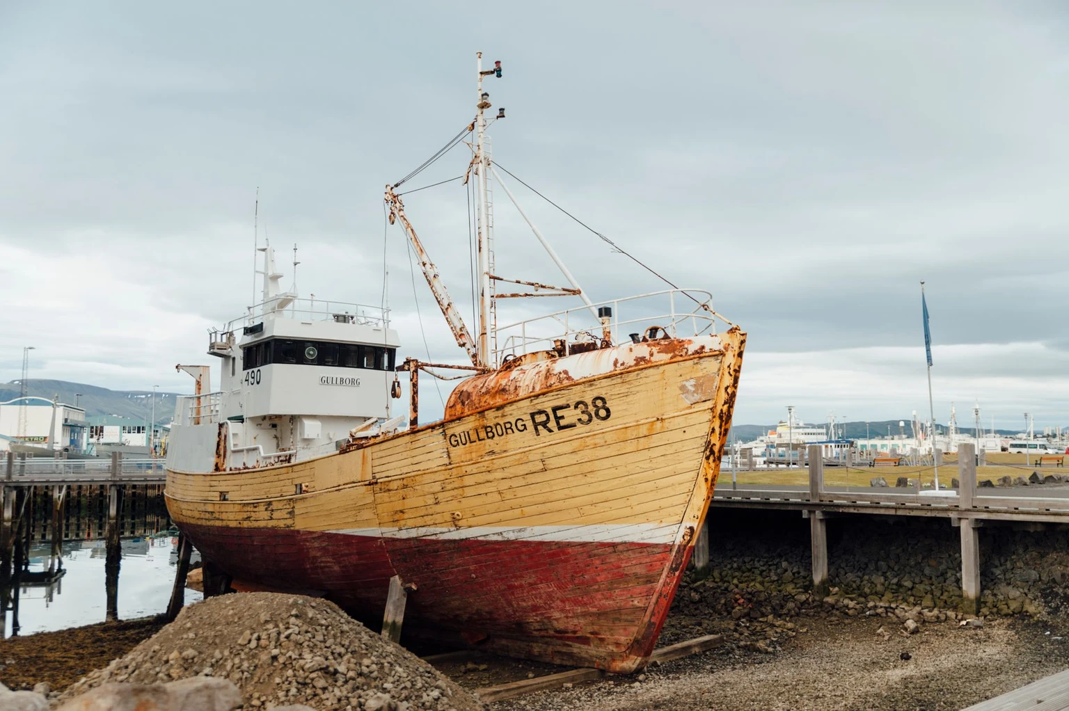 A weathered wooden fishing boat hauled up at Reykjavík's old harbor under a cloudy sky.