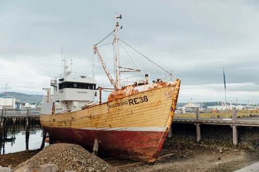 A weathered wooden fishing boat hauled up at Reykjavík's old harbor under a cloudy sky.