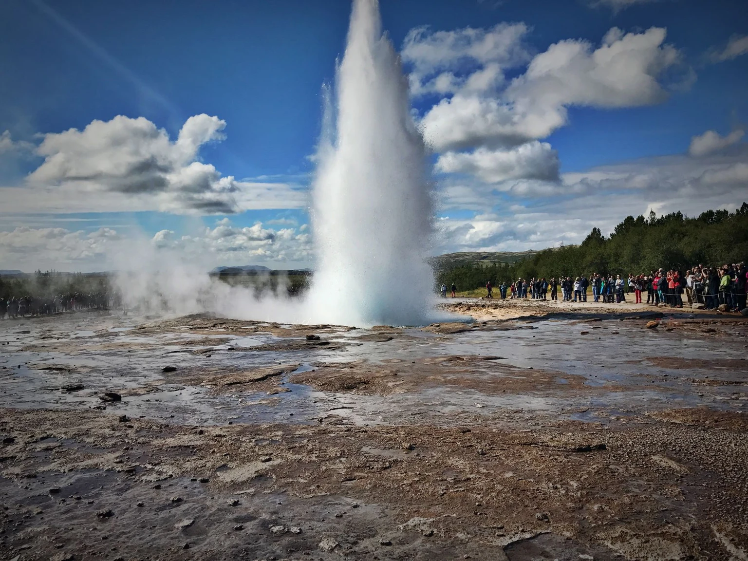 Dramatic geyser eruption in Iceland with tourists watching nature's force up close.
