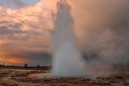 A stunning geyser eruption capturing the vibrant colors of sunset amidst the rugged landscape.