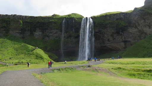 Stunning view of Seljalandsfoss waterfall with tourists amid Iceland's lush summer landscape.