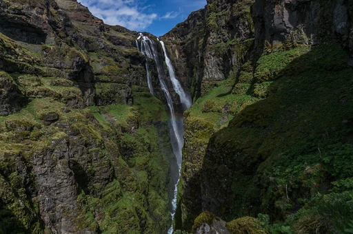 A tall, thin waterfall dropping through a green moss-covered canyon on a sunny day in south Iceland. Stand-in for Gljúfrabúi: place not confirmed from the source.