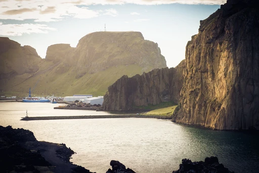 A tranquil coastal harbor surrounded by majestic cliffs and calm waters in Icelandic landscape.