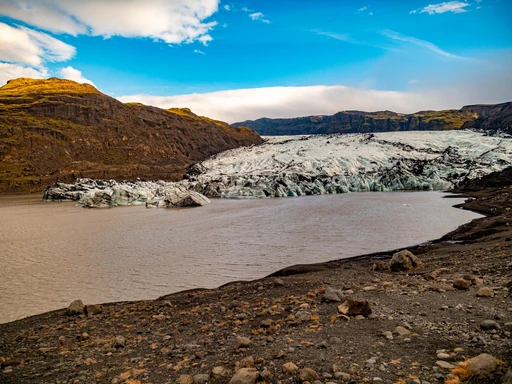 Scenic view of Solheimajokull glacier surrounded by rugged terrain under a vibrant sky.