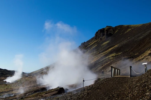 Steam rising from the hillside beside the path in the Reykjadalur valley, Iceland, under a blue sky.