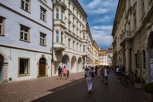 A cobblestone street in Bolzano with historic buildings and people walking.