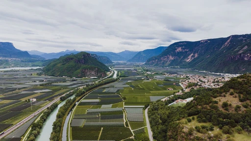 Aerial view of green fields in a wide valley below mountains near Bolzano.