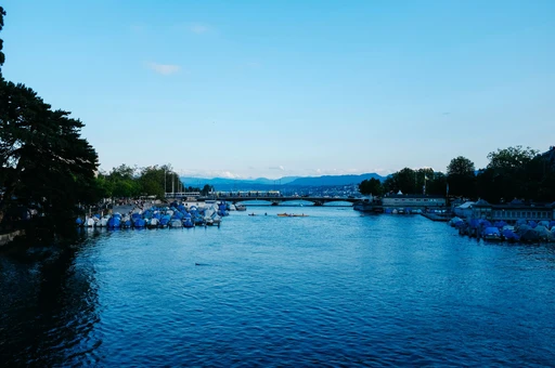 Picturesque view of Limmat River with moored boats and Zurich cityscape on a clear day.