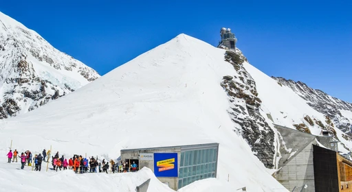 Visitors gathered outside the Jungfraujoch station buildings below the Sphinx Observatory, in bright snow under a blue sky.