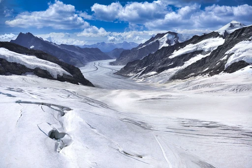 The Aletsch glacier seen from Jungfraujoch, a wide river of ice between rock ridges under a partly cloudy sky.