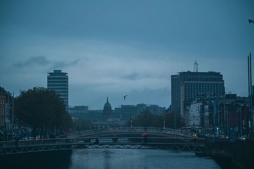 Moody Dublin cityscape showcasing Ha'penny Bridge over the Liffey River at dusk with an overcast sky.