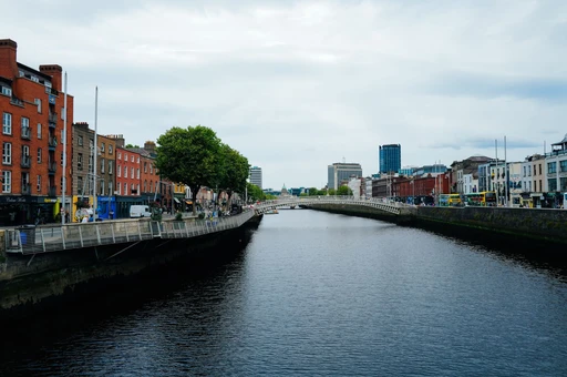 Scenic view of Dublin's Ha'penny Bridge over the River Liffey amidst urban architecture and vibrant city life.