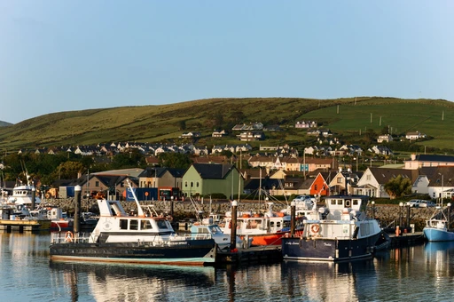 Picturesque view of boats docked at Dingle Harbor with lush hills in the background.