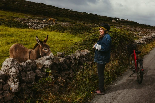 A woman stroking a donkey beside a stone wall on Inis Mór, with a hire bicycle leaning next to her.