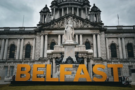 Large orange BELFAST letters standing in front of City Hall and its statue.