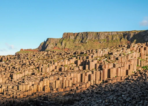 Hexagonal basalt columns of the Giant's Causeway in warm evening light, with the cliffs rising behind.