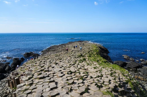 Walkers on the flat basalt stones of the Giant's Causeway, running out toward open sea under a clear sky.