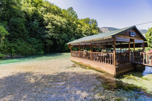 The clear stream flowing from the Blue Eye spring, with a timber restaurant terrace on the bank and forest behind.
