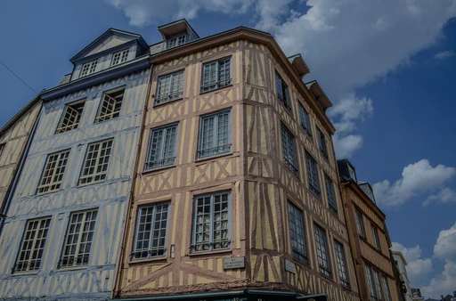 A half-timbered facade in Rouen under a blue sky with white clouds.