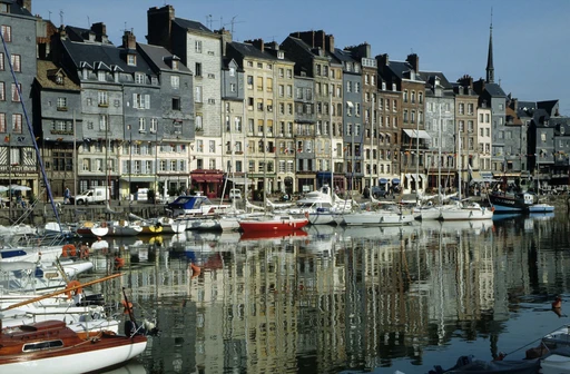 Boats moored in the Vieux Bassin in Honfleur, with tall narrow houses reflected in the water.
