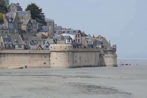 The ramparts and slate-roofed houses of Mont-Saint-Michel above the sand at low tide.
