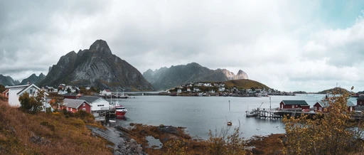 Panorama of Reine with red cabins, mountains and a calm fjord, Lofoten.