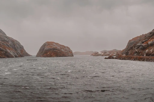 The narrow entrance to Nusfjord harbor between rounded rocks on a cloudy day, Lofoten.