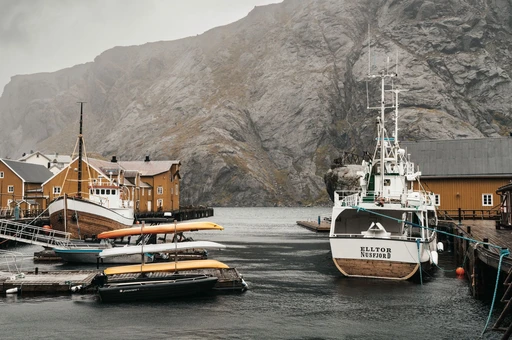 Fishing boats moored at the quay in Nusfjord below a rock face, Lofoten.