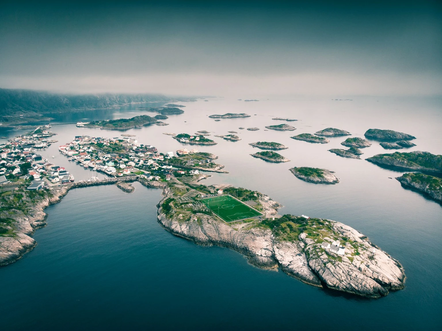 Aerial view of Henningsvær on its islands, with the football pitch on a rock in the foreground, Lofoten.