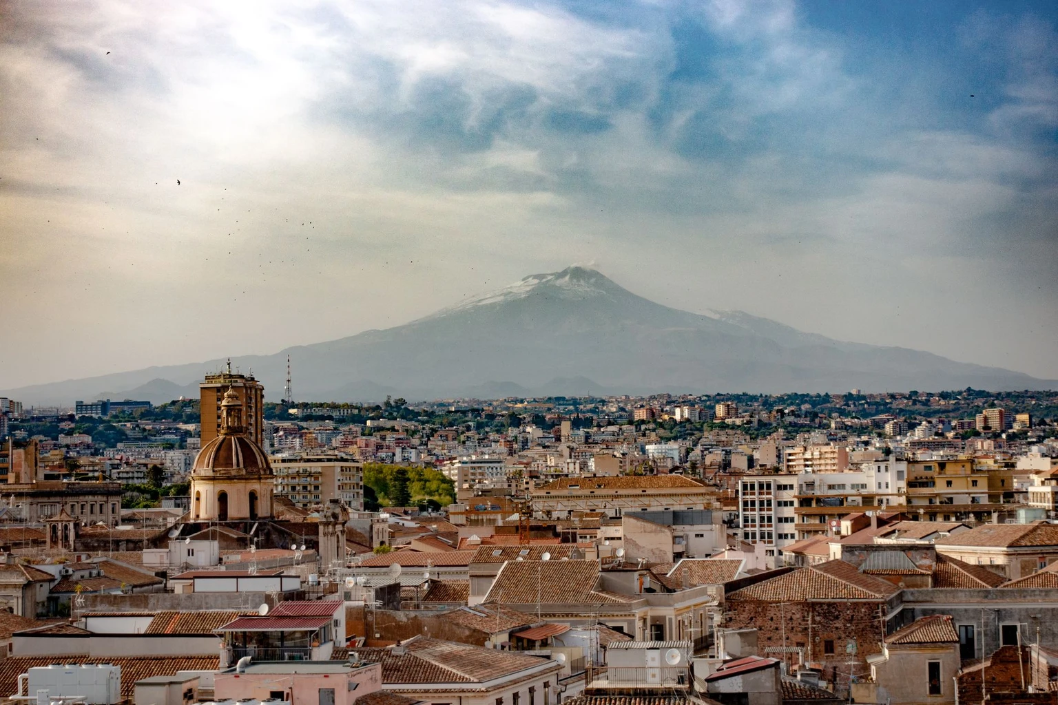 Rooftops of Catania with the cone of Mount Etna rising behind the city.