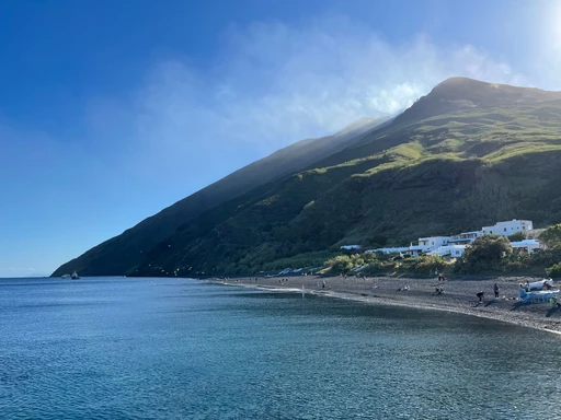 The black volcanic beach and white houses of Stromboli village under the green slope of the volcano.