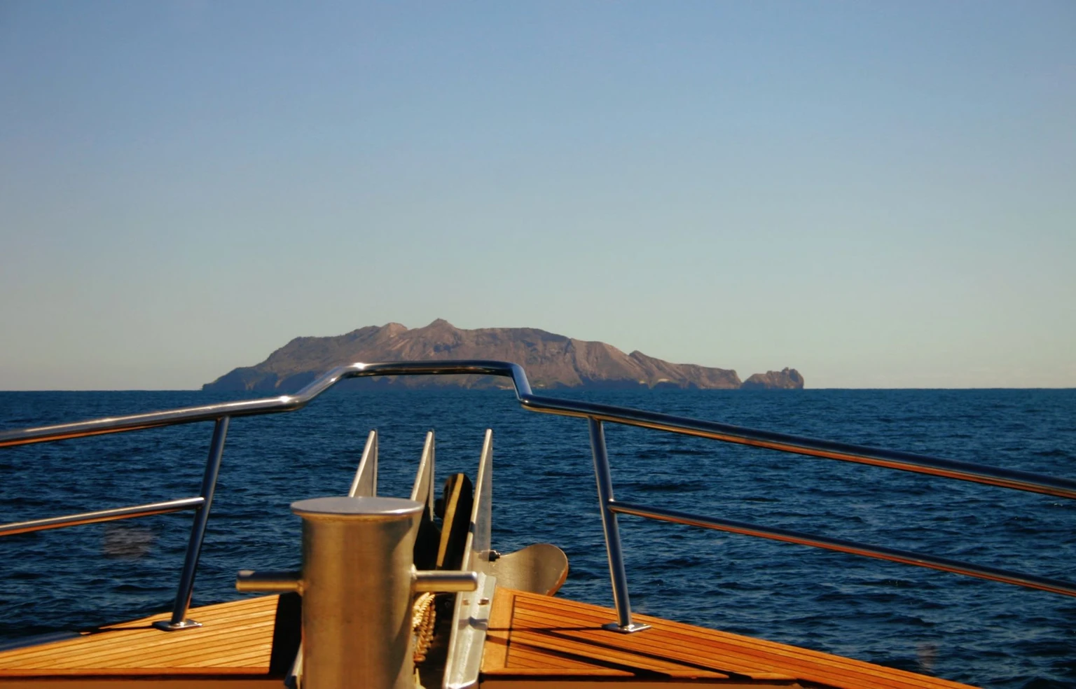 The bow of a boat heading across open sea toward a distant island.