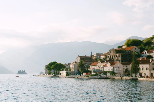 Stone houses along the waterfront of the Bay of Kotor, with the mountain wall rising behind the town.