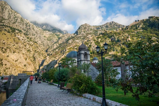 A stone path along Kotor's old walls, with a small church and the rocky mountainside above the town.