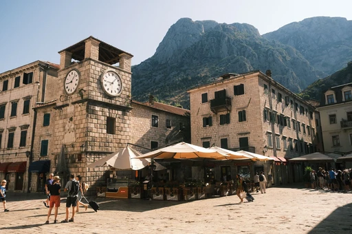 Kotor's old-town square with the clock tower and stone houses, seen in clear light.