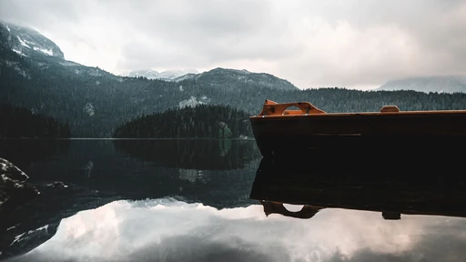 A wooden boat reflected in the still water of Black Lake, with Durmitor's mountains behind.