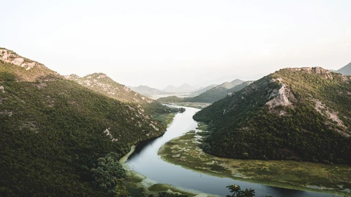 The Rijeka Crnojevica river winding between green hills toward Lake Skadar, with a small boat on the water.