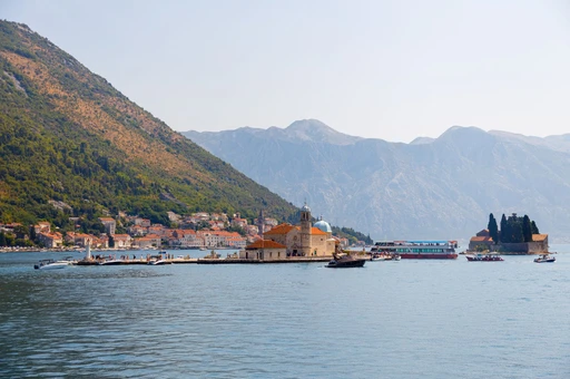 Our Lady of the Rocks island seen across the water, with Perast's shoreline and mountains behind.
