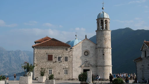 The front of the Church of Our Lady of the Rocks, a stone church with a tall bell tower and a pale blue dome.