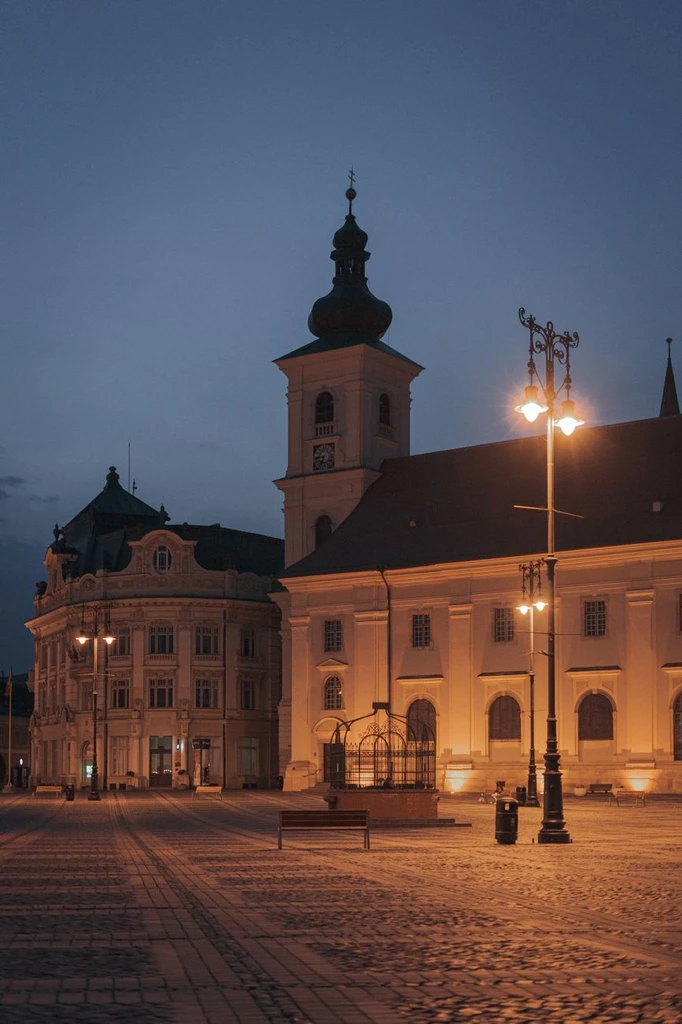 Sibiu's old buildings lit at twilight, with the town's narrow roofs and church spires.