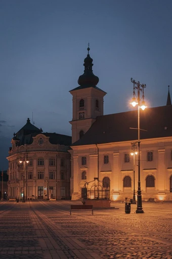 Sibiu's old buildings lit at twilight, with the town's narrow roofs and church spires.