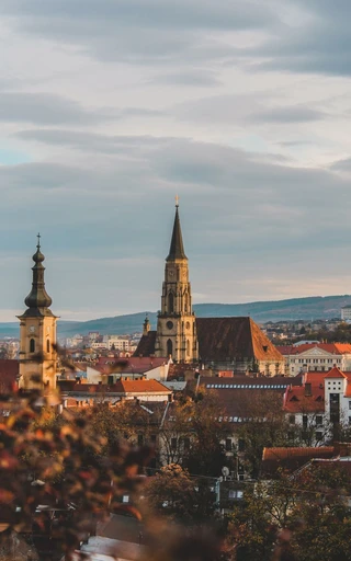 Cluj-Napoca at sunset, the city's rooftops and church spires lit in warm light.