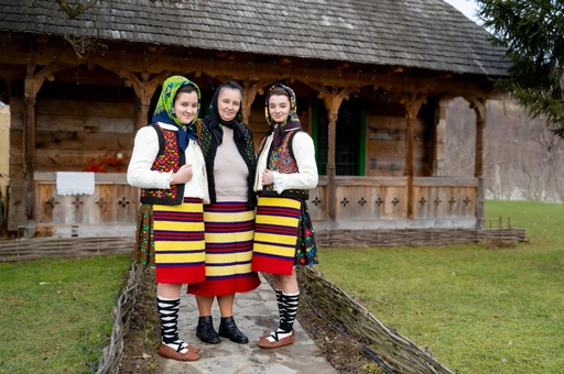 Three women in traditional Maramureș dress outside a wooden house. Not a dinner scene.