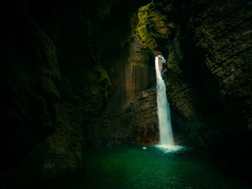 A waterfall dropping into a dark rock hall above a green pool in the Soča valley, Slovenia.
