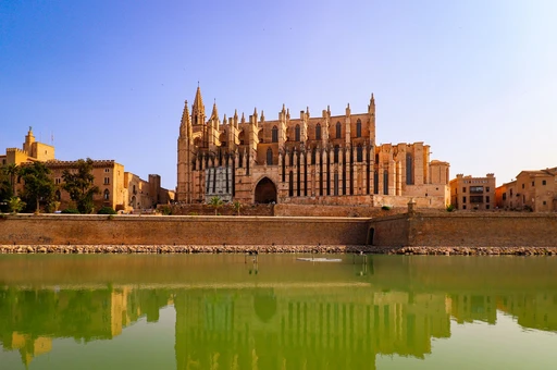 Palma Cathedral reflected in the water below the old sea wall in afternoon sun.