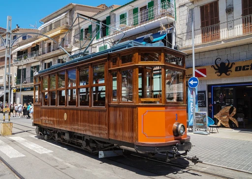 The wooden Sóller tram passing shopfronts on a town street.