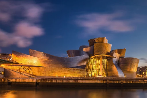 Dramatic evening view of the illuminated Guggenheim Museum in Bilbao along the riverbank.